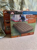 Front view of two Ozark Trail twin size vinyl air beds in original packaging, showing product image of one inflated air bed and outdoor tent scene.