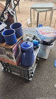 Photo showing blue enamel coffee pot and mugs atop Coleman DuraCat heater box, oil lamp and tarp visible behind