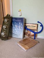 Photo of wooden thermometer with two glass dials, crystal chess and checker set in box, blue horseshoe-shaped exercise tool, wooden cutting board, and Christmas Village Advent calendar box.