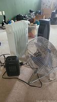 Four items include a metal fan, oil-filled radiator heater, ceramic heater, and tower heater placed together on carpet.