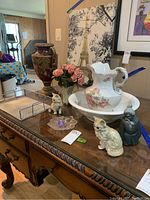 Photo of decorative urn, floral pitcher and bowl, cat figurines, paper tray and flowers on table