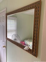 Beveled wall mirror hanging on a light-colored wall, showing the decorative oval pattern on the frame and beveled glass edges.