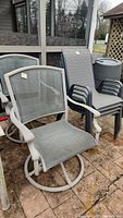 Two swivel metal-frame patio chairs and four stationary metal-frame patio chairs arranged outside, showing metal frames and mesh fabric seats in grey tone.