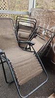 Three metal framed folding patio chairs stacked and one reclined; two chairs have canvas fabric, one has mesh. Image showing condition and style of seats and metal frames with wear.