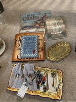 Lot overview showing Blue Crabs placemat, two wooden plaques with sayings, small ornate gold-tone tray, and a rectangular ceramic serving platter holding silver pieces.