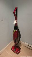 Full image of the red upright vacuum cleaner standing against the wall showing overall shape and condition.