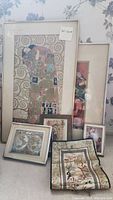 Five framed pieces of wall art and one embroidered Asian scarf leaning against a floral wallpapered wall, showing variety in style and size, captured to illustrate the items in the lot.