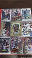 Nine autographed sports cards including football and basketball players arranged in a 3x3 grid on a dark surface.