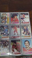 Photo showing 9 hockey cards in protective sleeves with players from teams such as Sabres, Red Wings, Barons, Bruins.