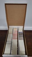 Photo of an open cardboard box showing three vertical stacks of trading cards in various back designs, colors, and wear.