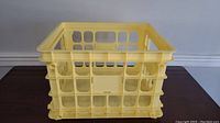 Yellow plastic record crate with open grid design, handles for carrying, and sturdy construction.