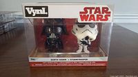 Front view of the Star Wars Vynl Darth Vader and Stormtrooper figurines in clear display packaging.