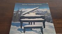 Front cover of Supertramp's 'Even In The Quietest Moments' vinyl album showing a snowy black grand piano outdoors with mountains in background.