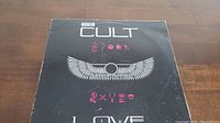 Front cover of The Cult Love vinyl album showing band's name and winged symbols.