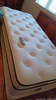 Photo showing the full mattress top with remote control on it, highlighting the fabric and tufted organic cotton material.