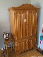 Front view of the solid oak 4-door cabinet showing four paneled doors with decorative arch tops and a curved crown molding at the top.