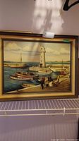 Framed painting depicting Donag Hadee Harbour with a lighthouse, boats and people, signed by Joyce Voteary dated 1974. Minor frame damage visible.