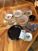 Overview of nine ashtrays on wooden surface, mixed glass and ceramic with various shapes and colors