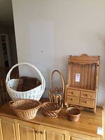 Photo of the wall cabinet alongside the six different woven baskets arranged on a wooden surface, showing size and style variety.