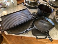 Cast iron cookware arranged on countertop, showing rectangular griddle, two grill pans, and large round oven pan.