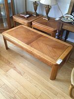 Photo showing pair of matching square end tables with decorative lamp bases and partial view of coffee table in front. Wood finish and brass accents visible.