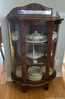 Full front view of curved glass curio cabinet with interior shelves and contents