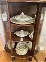 Wood cabinet with shelves holding Wood And Son semi porcelain dishware including plates, saucers, tureens, and teacups.