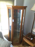 Front right angle view of oak corner display cabinet showing wood frame, glass door and shelves