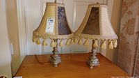 Photo showing two plaster-based lamps with beige, blue, and gold fabric shades on a wooden table.