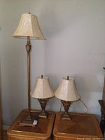 Set of one floor lamp and two matching table lamps, all with gold-colored classical design bases and cream floral fabric shades