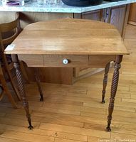 Full view of solid wood occasional table showing oval shape and top surface with drawer beneath and spindle legs.