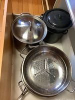 Granite Ware black speckled stock pot with metal lid and steel blancher drainer insert, placed inside a drawer.
