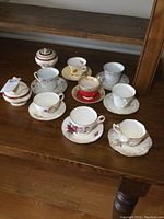 Photo displaying 8 teacups with matching saucers and a cream and sugar set on wooden shelf.
