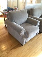 Pair of gray oversized arm chairs positioned side by side, showing front and angled side views, highlighting rolled arms and cushioned backs.