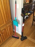 Photo showing the vacuum cleaner standing upright next to the broom and dustpan on wood floor.