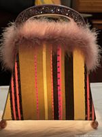 Front view of the purse-shaped lamp showing striped fabric, sequin decoration, and pink feather trim along top edge.