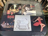 Photo showing all five LP records laid out on a glass table outdoors, including album cover artwork showing different artists and styles.