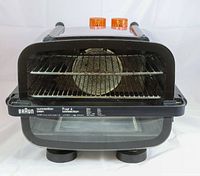 Front view of Braun convection oven showing glass door, interior with wire racks, fan, and orange control knobs on top.