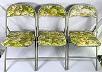 Front view showing three identical green metal folding chairs in a row with floral vinyl seats and backs.