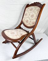 Side angled view showing the hand-carved floral top, floral upholstery, mahogany wood frame, and rocking base.