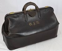 Front view showing black long grain leather travel bag with two leather handles, brass lock mechanism, and gilt initials 'C.S.M.'