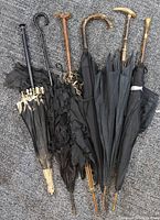 Six antique and vintage umbrellas/canes laid side by side vertically on carpet background showing handles and closed canopies.