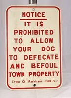 Front-facing image of the cream-colored metal sign with red text showing a dog defecation prohibition notice for Town of Markham bylaw 75-71. The sign measures 12 inches by 18 inches and has mounting holes at top and bottom.