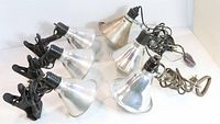 Six clip-on lamps with spun metal shades, arranged to show the lamps and clamps (plastic and wire clamps) including cords and plugs.