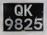Front view of a vintage 1940's British license plate with black background and silver raised characters reading QK 9825. Manufacturer 'Hills' marked below center.