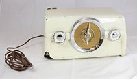 Front view showing cream Bakelite radio with chrome knobs and original fabric grill on the central speaker dial.