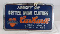 Front side of metal sign showing Carhartt branding and union made work clothes promotion with blue background and white and red text.