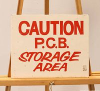 Front view of the metal sign showing red screen printed text on white enamel background reading 'CAUTION P.C.B. STORAGE AREA'.