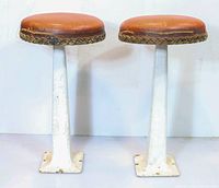 Full view of two vintage diner stools with cast metal white bases and tan round seats.