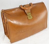 Front angled view of the tan leather A frame briefcase with brass lock and handle showing overall shape and wear.
